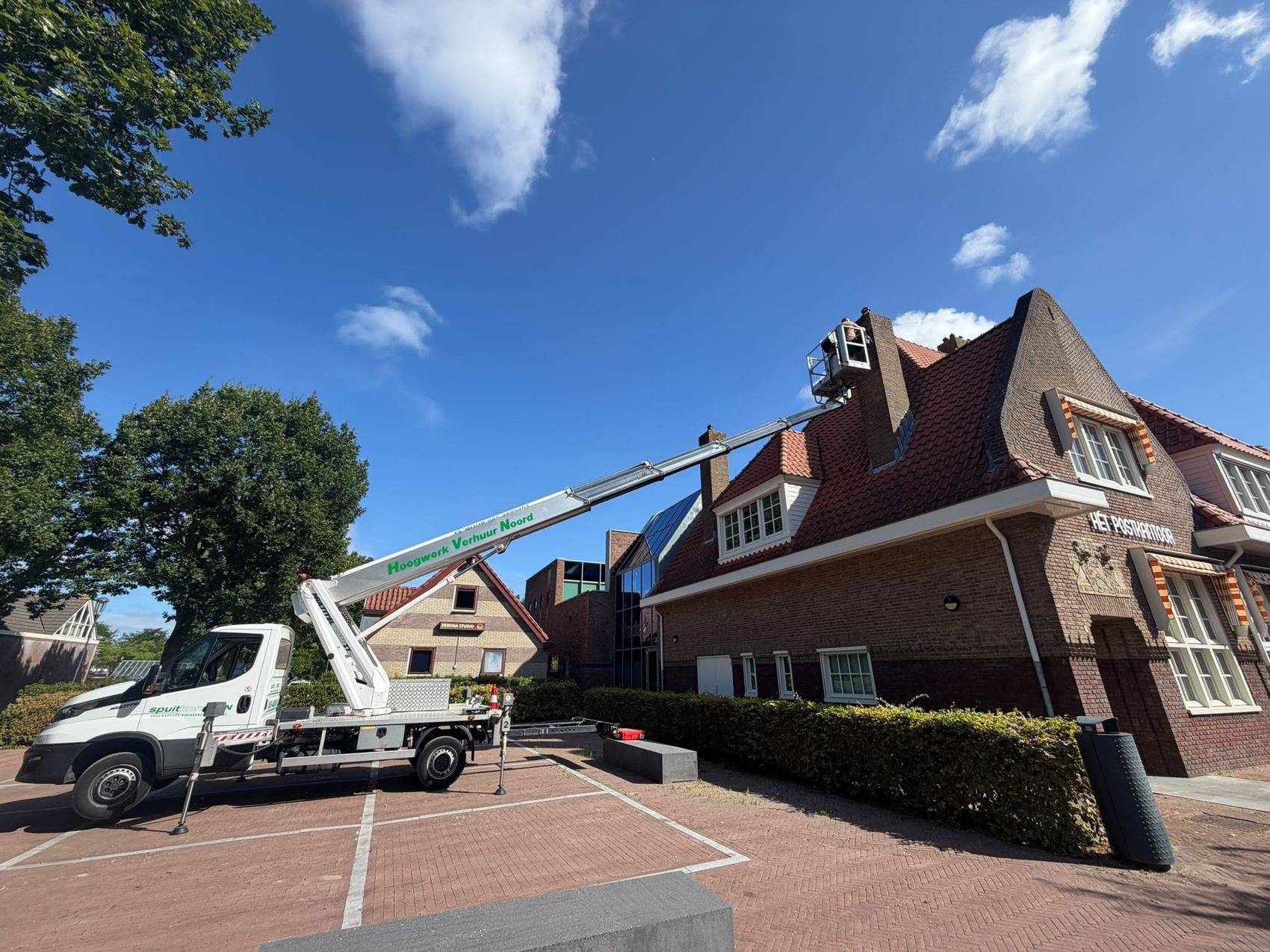 Hoogwerker opgesteld bij een monumentaal pand, met een medewerker bij de dakrand