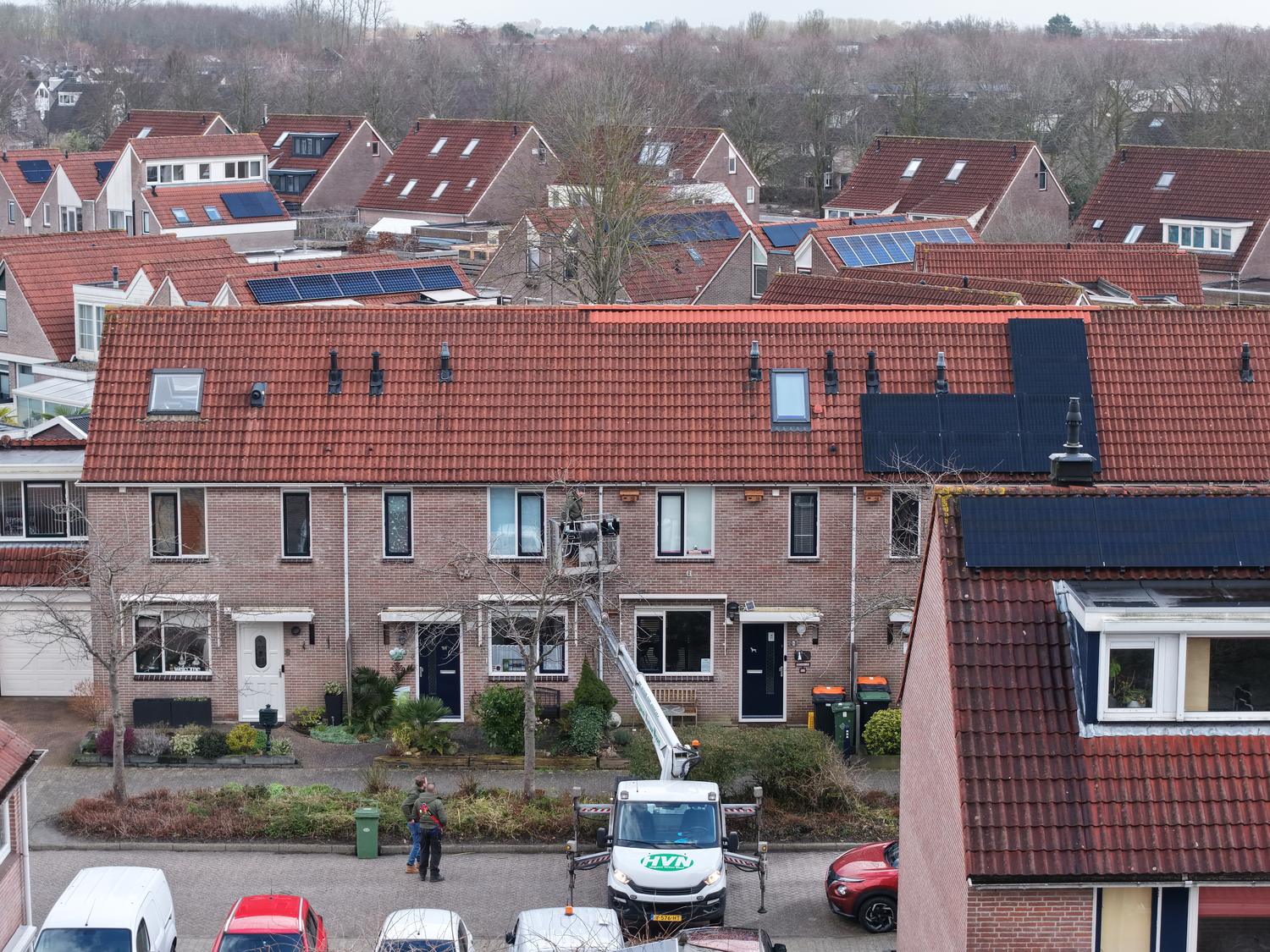 Luchtfoto van een rij woningen met een hoogwerker die bij de dakrand werkt